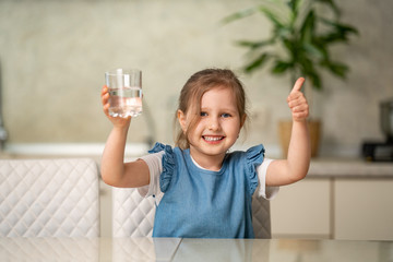 Cute little girl drinking water in kitchen at home. Prevention of dehydration