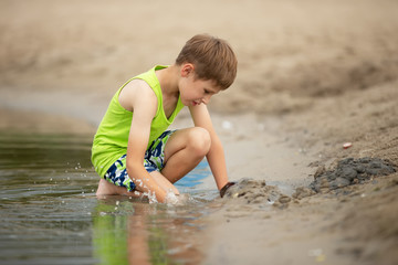 A boy plays with the sand on the lake on a cloudy summer day.
