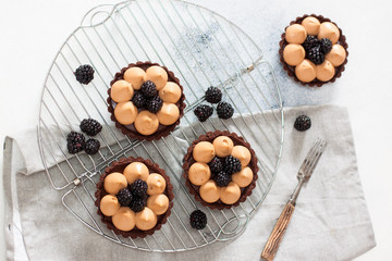 Blackberry tarts with whipped cream and chocolate filling on metal cooling rack. Grey background.