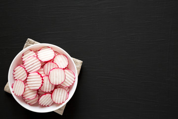 Fresh Radish Chips Slices in a white bowl on a black background, top view. Flat lay, overhead, from above. Copy space.