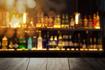 black wood table with blur alcohol drink bottle at pub or bar in dark night interior background
