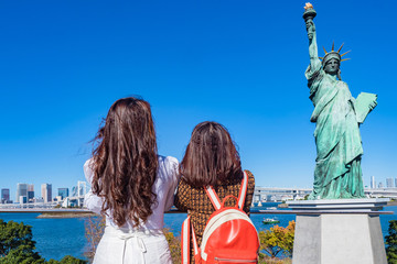 Japan. Statue of liberty on Odaiba island. Two girls look at the Statue of Liberty in Tokyo. Attractions of the Japanese capital. Women and a statue against the blue sky. Monuments Of Tokyo.