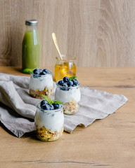 Healthy breakfast set with coffee, homemade yogurts with granola and blueberries, honey and green juice. 