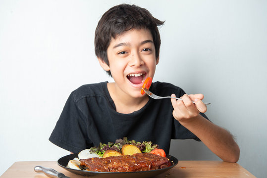Little boy teenager eating tomato with salad for his meal