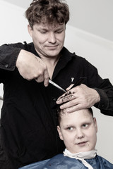 Hairdresser cuts the hair of a boy with scissors