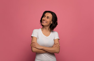 Obraz premium After a good nap. Attractive woman in white t-shirt is looking to the left upper corner, while smiling with folded arms.