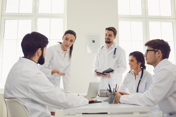 Group of practicing doctors in a meeting discuss the diagnosis of a patient standing in a clinic...
