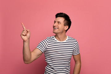 My favourite view. Close-up photo of cheerful young man in a striped t-shirt, who is smiling while pointing to the left upper corner.