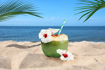 Green coconut with refreshing drink and beautiful flowers on sandy beach near sea