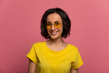 A portrait. Close-up photo of a lovely young girl with short haircut, in yellow outfit and stylish sunglasses, who is looking in the camera and smiling.