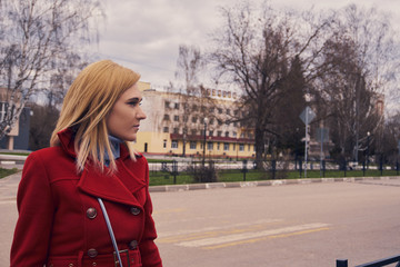 A beautiful girl in a red coat looks into the distance at the empty streets. Thoughtful look, freedom of thought.