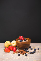 Oatmeal with blueberries and strawberries in a wooden plate. Peaches and berries on the table. Black background with a place for text. 