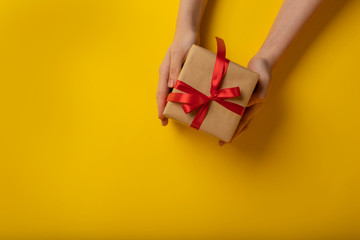 Woman holds a parcel on a yellow background. Gift giving concept.