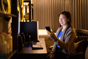 Happy young Asian woman using phone while working from home