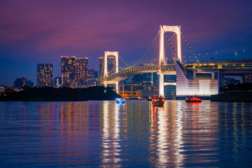 Fototapeta na wymiar Japan. Boating on Tokyo Bay at sunset. Rainbow bridge on the background of the evening city. White suspension bridge in Japan. Attraction In Tokyo. The Island Of Odaiba.
