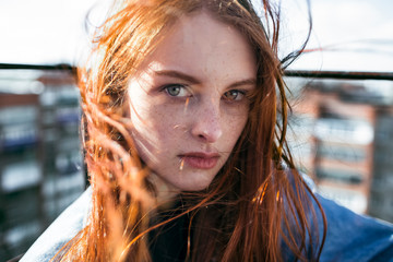 A girl with red hair on a roof with a strong wind