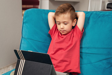 Little boy sitting on sofa and playing on digital tablet