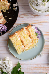 Biscuit cake with cream, impregnated with coconut and pineapple, decorated with lilac flowers.