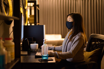 Young Asian woman with mask working from home late at night