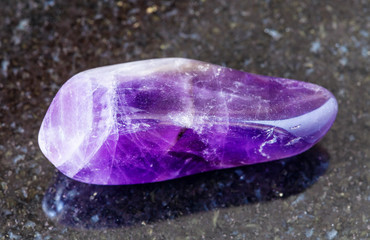 closeup of sample of natural mineral from geological collection - polished Amethyst rock on black granite background from Namibia