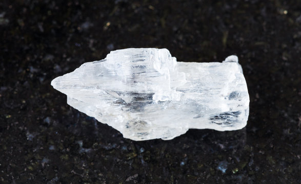 closeup of sample of natural mineral from geological collection - rough Petalite rock on black granite background from Araguai, Brazil