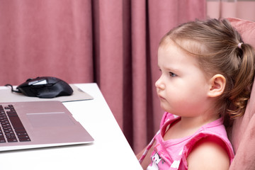 Beautiful cute sad little girl at a laptop. The concept of the dependence of children on computer games, cartoons and gadgets.