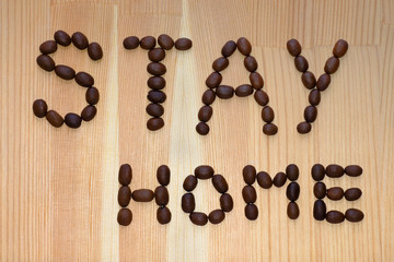 Lettering stay home sign made of roasted dark coffee beans on light brown wooden background. Every morning during quarantine, staying at home and drink aromatic coffee to improve your mood