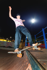 A young skater does the trick of sliding at night in a skatepark amid the burning lights of...