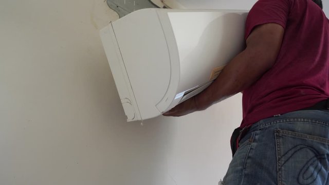 Technician removing air conditioner from wall for cleaning