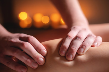 Close-up professional calf muscle massage to a female client by a male physiotherapist in a massage parlor in a dark office against the background of burning candles