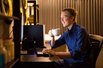 Happy young handsome businessman drinking coffee while working overtime at home