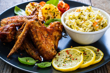 Roast chicken wings with potatoes and vegetable salad on wooden board
