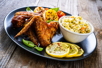 Roast chicken wings with potatoes and vegetable salad on wooden board
