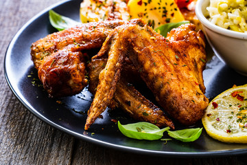 Roast chicken wings with potatoes and vegetable salad on wooden board
