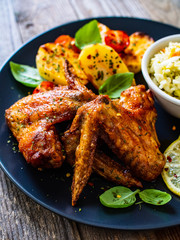Roast chicken wings with potatoes and vegetable salad on wooden board
