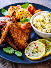 Roast chicken wings with potatoes and vegetable salad on wooden board
