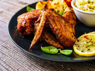 Roast chicken wings with potatoes and vegetable salad on wooden board
