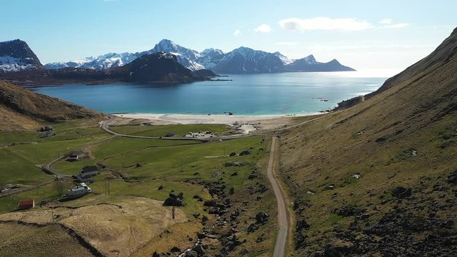 Aerial drone footage of haukland beach from a distance with mountains in background. Road leads to the beach. summer day. located norway, lofoten islands