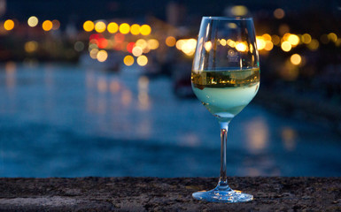 Weißweinglas steht auf Brückengeländer vor einem Bokeh-Hintergrund während der Blauen Stunde