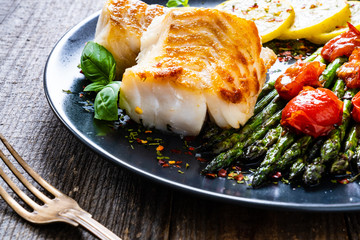 Fish dish - fried cod fillet with asparagus on wooden table
