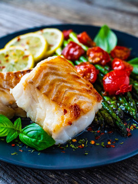 Fish dish - fried cod fillet with asparagus on wooden table
