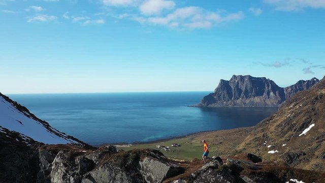 aerial video of trail runner man running on the ridge of mountain with incredible view over beach and mountains. Located norway, lofoten islands at haukland beach and mannen mountain.
