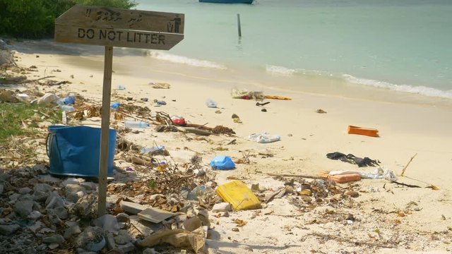 CLOSE UP: Littering sign stands in middle of a dirty beach in Maldives. Wooden sign prohibits littering on a white sand beach full of garbage the ocean flooded onto the once pristine tropical island.