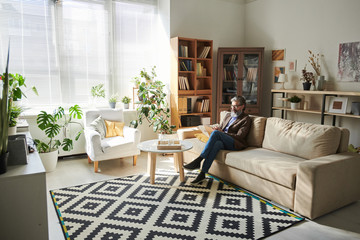 Contemporary senior professional psychotherapist sitting on couch by table