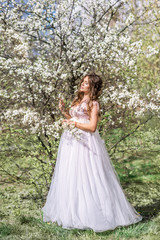 Fototapeta na wymiar beautiful pregnant woman in a long light dress walks in a blooming spring garden in the spring garden