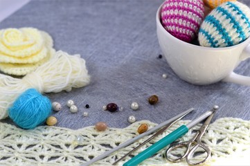 Fototapeta na wymiar Crochet flowers and eggs with hooks scissors and beads on grey background.
