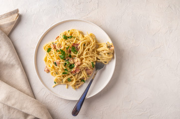Classic homemade pasta carbonara Italian with bacon, eggs, parmesan cheese on light ceramic plate with fork and napkin on light table. Copy space