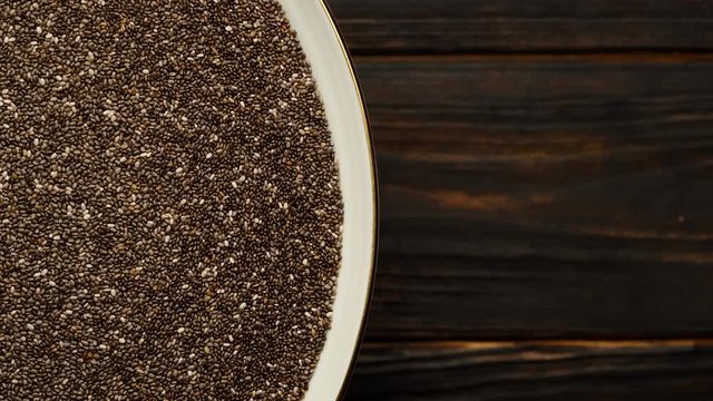 superfood chia seeds in white plate rotating top view . dark wooden background. place for text