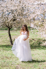 Obraz na płótnie Canvas beautiful pregnant woman in a long light dress walks in a blooming spring garden.