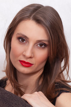 Close up portrait of middle aged attractive woman with beautiful almond-shaped brown eyes and thick eyebrows, bright red lipstick and smoky make up. Oriental type of beauty, black dress, ironic face.